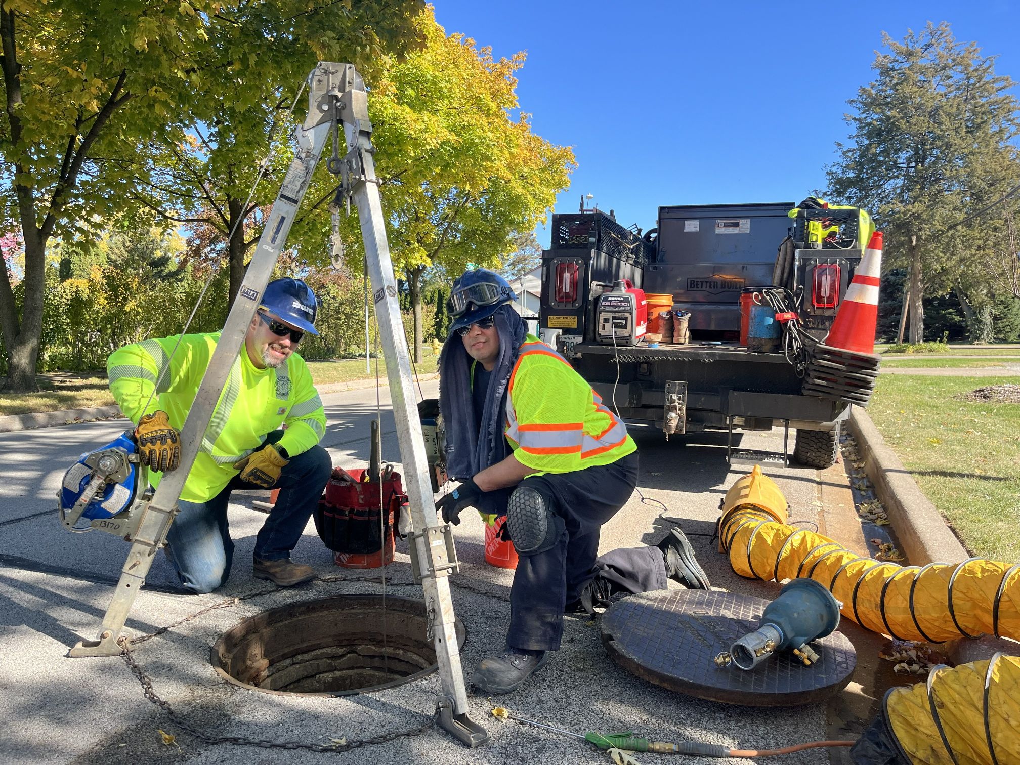 two people kneeling by manhole with safety setup